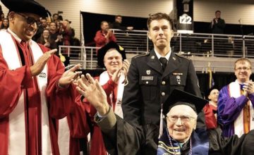 grandson stands behind his grandfather at graduation